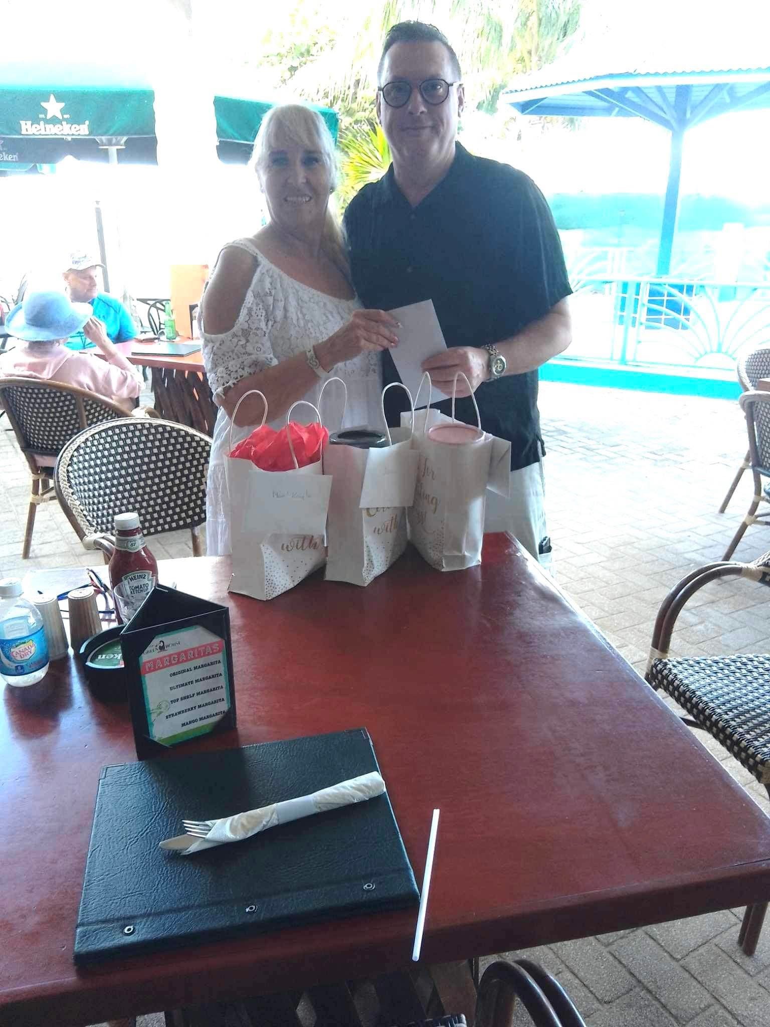 Two adults standing together behind a table of gift bags at an outdoor restaurant